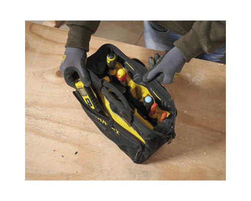 Eine Person mit Arbeitshandschuhen öffnet eine schwarz-gelbe Werkzeugtasche aus Stoff mit Handwerkzeugen auf einer hölzernen Werkbank.