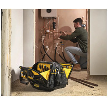 Offene Stanley Fatmax Werkzeugtasche im Vordergrund, Handwerker arbeitet im Hintergrund an Heizungsrohren.