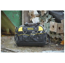 Stanley Fatmax Werkzeugtasche mit mehreren Außentaschen, Tragegriff und Schultergurt auf nassem Untergrund neben Metallbauteilen. Stanley Logo.