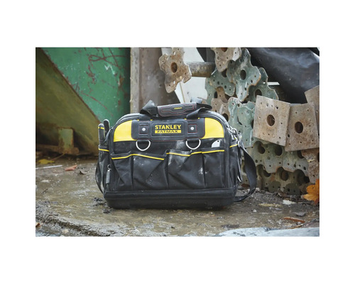 Stanley Fatmax Werkzeugtasche mit mehreren Außentaschen, Tragegriff und Schultergurt auf nassem Untergrund neben Metallbauteilen. Stanley Logo.