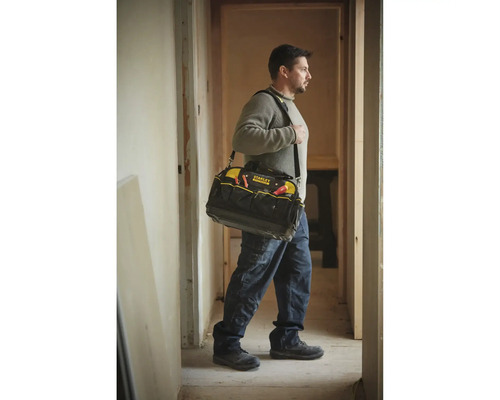 Handwerker trägt eine Stanley FatMax Werkzeugtasche mit Schultergurt in einem hellen Flur während Renovierungsarbeiten.
