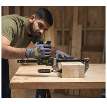 Stanley Fatmax Einhandzwinge fixiert Holzbalken auf einer Werkbank in einer hellen Werkstatt. Ein Mann mit Handschuhen bedient das Werkzeug.