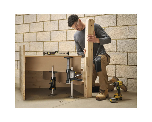 Handwerker montiert Holzkonstruktion mit Stanley Einhandzwinge, Wasserwaage und Akkuschrauber vor einer gemauerten Wand.