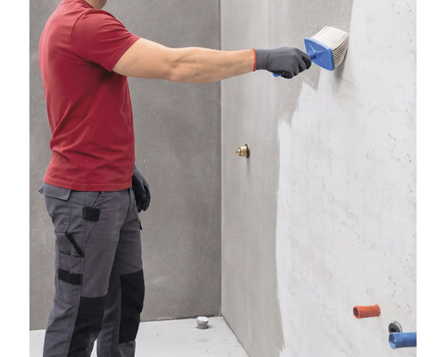 Person trägt mit einem Quast eine Wandgrundierung auf eine graue Wand auf.