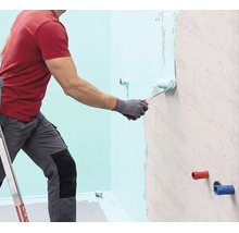 Eine Person trägt mit einer Farbwalze eine Flüssigabdichtung auf eine Wand auf.