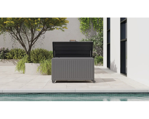 Offene graue Gartenbox aus Metall mit Rollen und Holzgriff auf einer hellen Terrasse neben einem Pool.