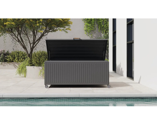 Moderne dunkelgraue Garten-Auflagenbox aus Metall mit Rollen und offenem Deckel, auf einer Terrasse neben einem Pool und Pflanzen.