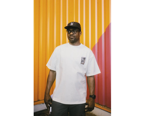 Mann trägt ein weißes Oversized T-Shirt aus Baumwolle mit Logo auf der Brust und eine schwarze Kappe.