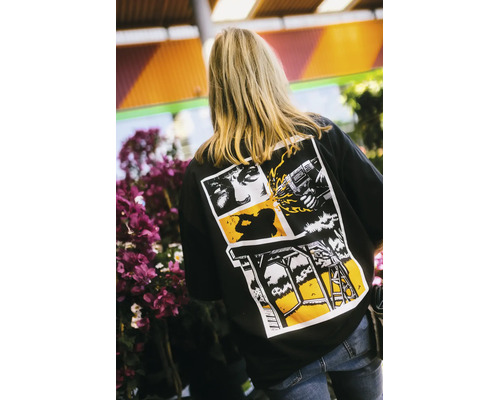 Rückansicht einer Person mit einem schwarzen T-Shirt mit grafischem Heimwerker-Print im Comic-Stil, der eine Bohrmaschine und ein Holzbauprojekt zeigt.