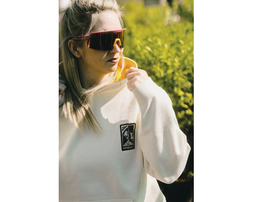 Frau mit hellem Kapuzenpullover mit Hornbach Logo und Sportsonnenbrille in heller Umgebung im Freien.