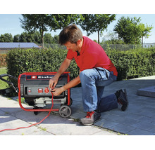 Ein Mann kniet auf einer Terrasse und schließt ein Kabel an einen fahrbaren Einhell Stromerzeuger an.
