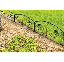 Dekorativer Metall-Gartenzaun mit Vogel- und Ast-Motiv, trennt ein Beet mit Rindenmulch von einer Rasenfläche.