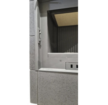 Detailansicht eines Kamineinsatzes mit Metallrahmen und geriffeltem Innenraum, eingefasst in gesprenkelte Fliesen.