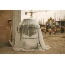 Betonmischer auf einer Baustelle, abgedeckt mit einer transparenten Schutzplane, neben einer Schaufel und einer Ziegelwand.