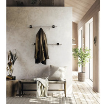 Moderne Wandgarderobe mit zwei Edelstahlstangen im hellen Vorzimmer mit Holzelementen, einer Sitzbank und Zimmerpflanze.