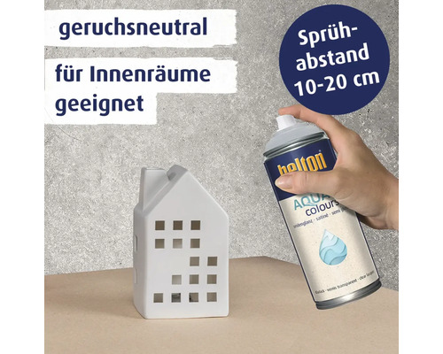 Eine Hand hält eine Belton Aqua Colours Klarlack Sprühdose zum Lackieren eines weißen Keramikhausmodells.