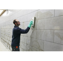 Handwerker beim Verfugen einer gefliesten Wand mit einem Fugenbrett und Schutzhandschuhen