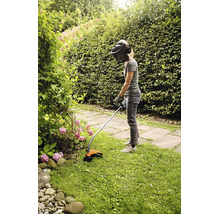 Eine Person benutzt einen Stihl Rasentrimmer mit Schutzvisier und Gehörschutz, um Kanten in einem Garten zu schneiden.