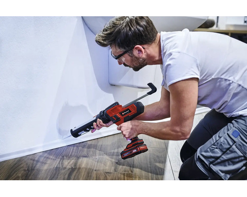 Ein Handwerker nutzt eine kabellose Einhell Akku Kartuschenpistole, um eine Fuge an einer Wandleiste abzudichten.