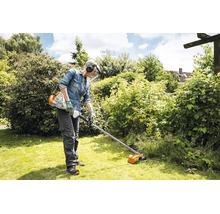 Eine Person benutzt einen Stihl Motorsensen Freischneider zur Rasenpflege in einem Garten mit schützender Arbeitskleidung und Gesichtsschutz.