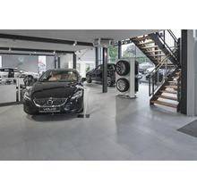 Modernes Volvo Autohaus mit Ausstellungsfahrzeugen, Reifenständer und einer Treppe in einer hellen, weitläufigen Verkaufsfläche mit Fliesenboden.