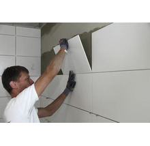 Handwerker beim Anbringen von großformatigen Fliesen an einer Innenwand mit Fliesenkleber.