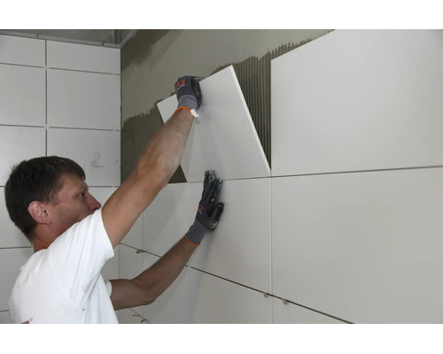 Handwerker beim Anbringen von großformatigen Fliesen an einer Innenwand mit Fliesenkleber.