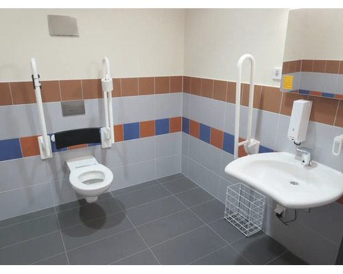 Barrierefreies Badezimmer mit wandhängendem WC, Stützklappgriffen, Waschbecken, Seifenspender und Kacheln in verschiedenen Farben.