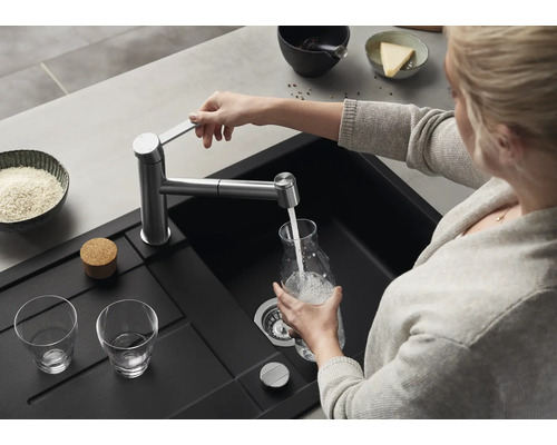 Eine Person füllt eine Glaskaraffe mit Wasser aus einer modernen Küchenarmatur über einem schwarzen Einbauspülbecken in einer Küche.
