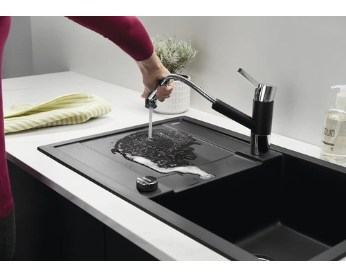 Eine moderne schwarze Küchenspüle mit ausziehbarer Küchenarmatur, an der eine Hand Wasser über die Abtropffläche fließen lässt.