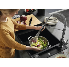 Person wäscht Salat in einem Metallsieb in einer schwarzen Einbauspüle mit ausziehbarer Küchenarmatur und Spiralfeder in einer modernen Küche.