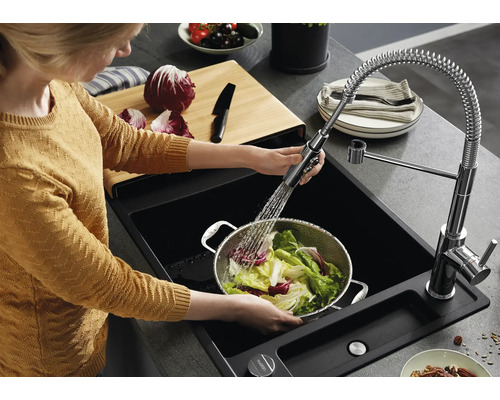 Person wäscht Salat in einem Metallsieb in einer schwarzen Einbauspüle mit ausziehbarer Küchenarmatur und Spiralfeder in einer modernen Küche.