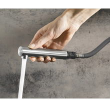 Hand hält eine ausziehbare Küchenarmatur mit fließendem Wasser aus einem flexiblen Schlauch.