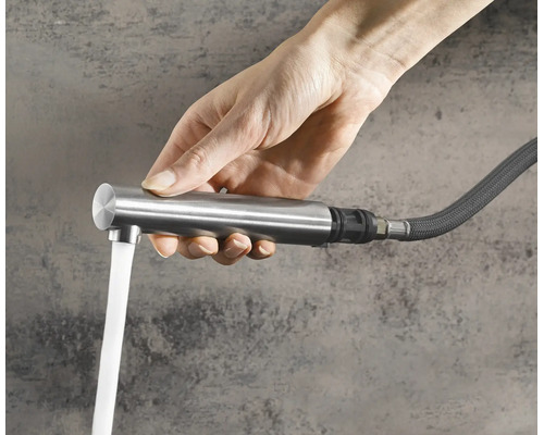 Hand hält eine ausziehbare Küchenarmatur mit fließendem Wasser aus einem flexiblen Schlauch.