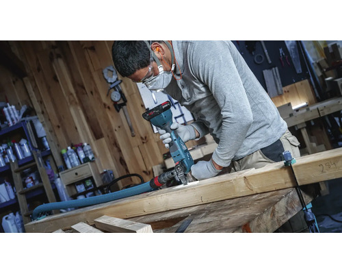 Handwerker bei der Arbeit mit einem oszillierenden Multifunktionswerkzeug mit angeschlossenem Absaugschlauch in einer Holzwerkstatt.