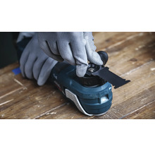 Eine Person mit Schutzhandschuhen wechselt das Sägeblatt eines oszillierenden Multifunktionswerkzeugs auf einer Werkbank.
