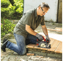 Handwerker mit Schutzkleidung nutzt Akku Handkreissäge von Einhell um Holzdielen im Garten zuzuschneiden.