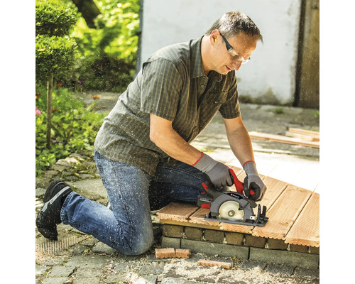 Handwerker mit Schutzkleidung nutzt Akku Handkreissäge von Einhell um Holzdielen im Garten zuzuschneiden.