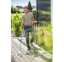Ein Mann benutzt einen Gas Unkrautbrenner auf einer gepflasterten Gartenfläche, um Unkraut zwischen den Steinen zu entfernen.