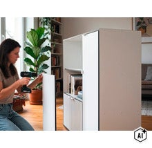 Eine Frau montiert einen modernen Schrank mit einem Akku Schrauber in einem Wohnzimmer. (Image AI modified or generated)