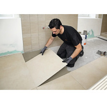 Handwerker beim Verlegen von großformatigen Fliesen auf einem vorbereiteten Fliesenkleberbett in einem Badezimmer.