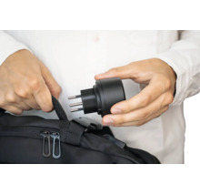 Eine Person hält einen Reiseadapter mit Stecker in der Hand über einer schwarzen Tasche.