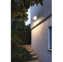 LED Außenwandleuchte mit Bewegungsmelder beleuchtet eine Treppe vor einer Hausfassade im Garten bei Dämmerung.