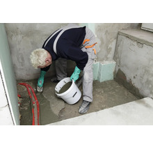 Handwerker bei der Verlegung von Estrich mit einer Glättkelle und einem Eimer auf einer Baustelle.