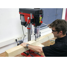 Einhell Tischbohrmaschine im Einsatz, wobei ein Handwerker mit Schutzbrille ein Holzstück bearbeitet.