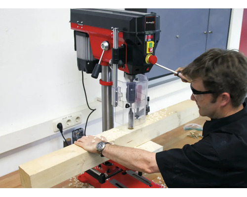 Einhell Tischbohrmaschine im Einsatz, wobei ein Handwerker mit Schutzbrille ein Holzstück bearbeitet.