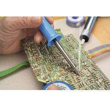 Eine Hand lötet mit einem Lötkolben ein elektronisches Bauteil auf eine grüne Leiterplatte.