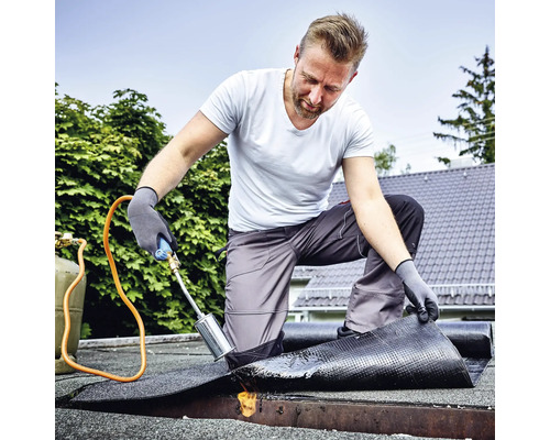 Handwerker beim Verschweißen von Bitumenschweißbahnen mit einem Gasbrenner auf einem Flachdach.