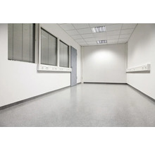 Leeres, funktionales Büro oder Gewerberaum mit weißen Wänden, grauem Bodenbelag, Rasterdecke und Fensterfronten mit Jalousien.