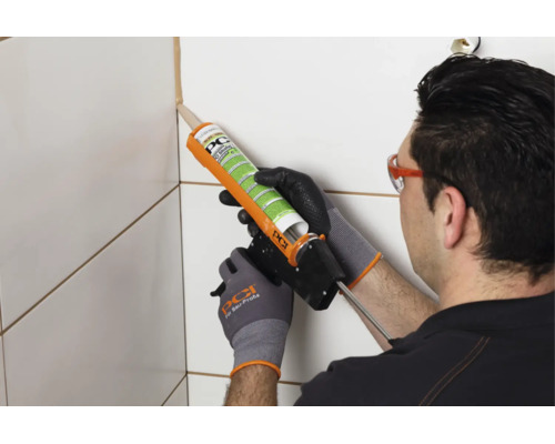 Ein Handwerker trägt mit einer Silikonpistole PCI Silicofug Dichtstoff in die Fliesenfuge auf.